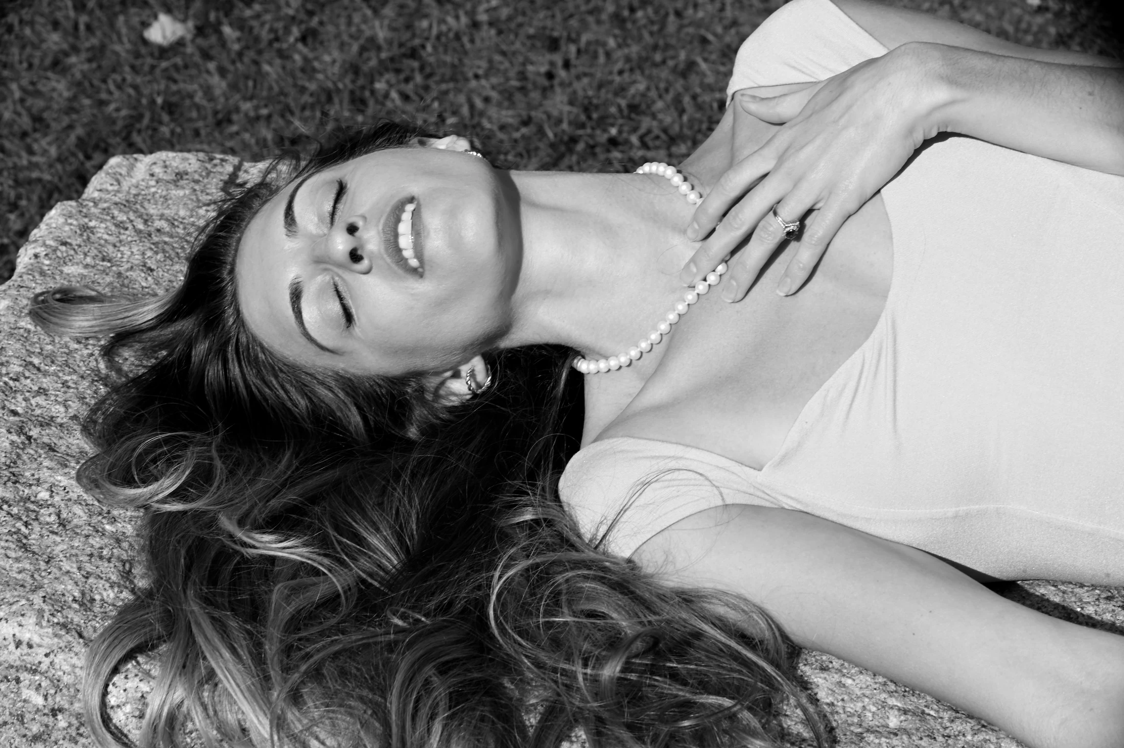 Black-and-white portrait of Marissa reclining outdoors, smiling with her eyes closed and a hand over her heart.