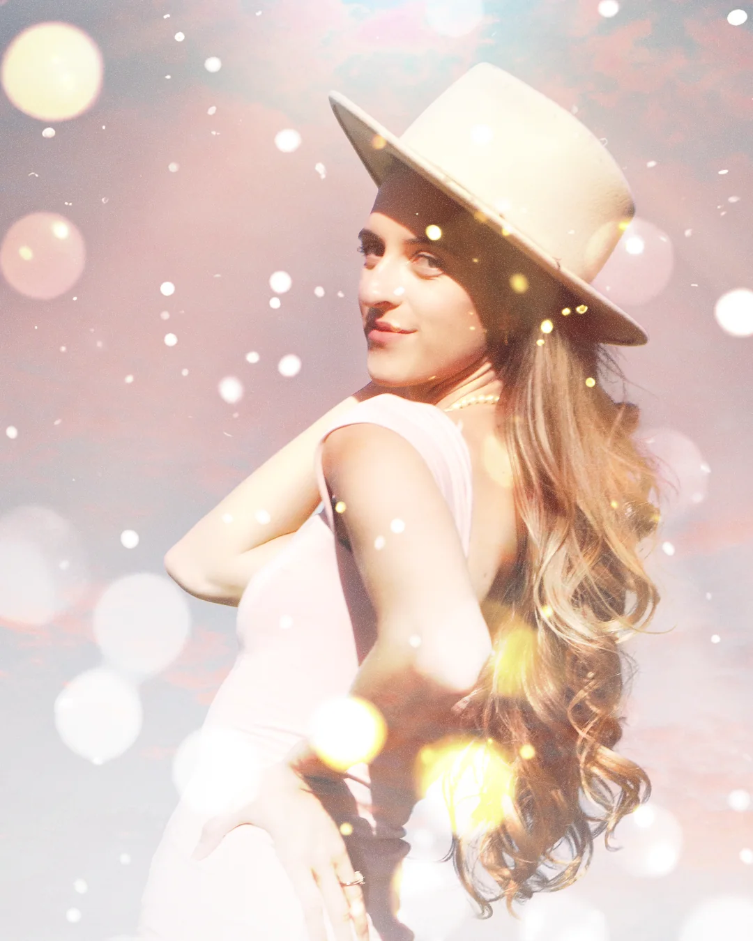 Marissa in a pale pink dress and wide-brimmed hat, surrounded by a soft overlay of light.