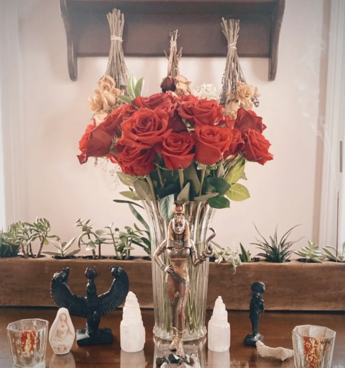 Red roses arranged on a candlelit altar with crystals and two dark figurines.