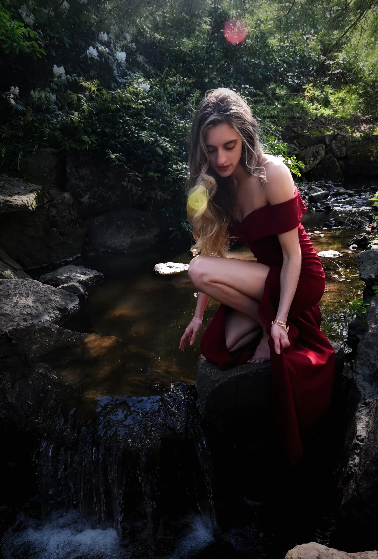Marissa in a red dress beside a wooded stream and small waterfall.